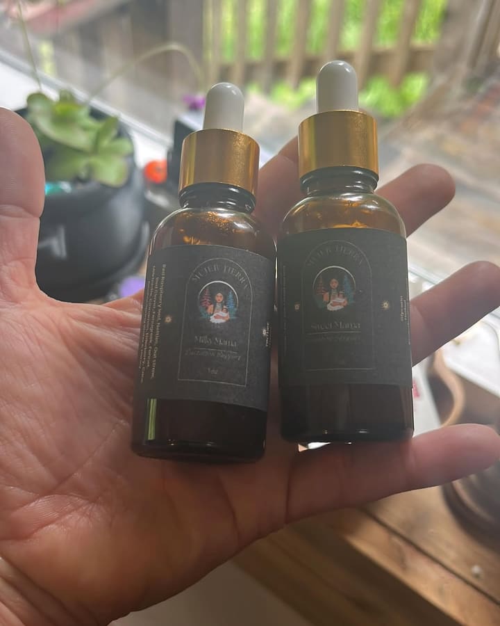 Two amber dropper bottles with gold caps and Mujer Tierra labels, held up outdoors, with no face in the frame.