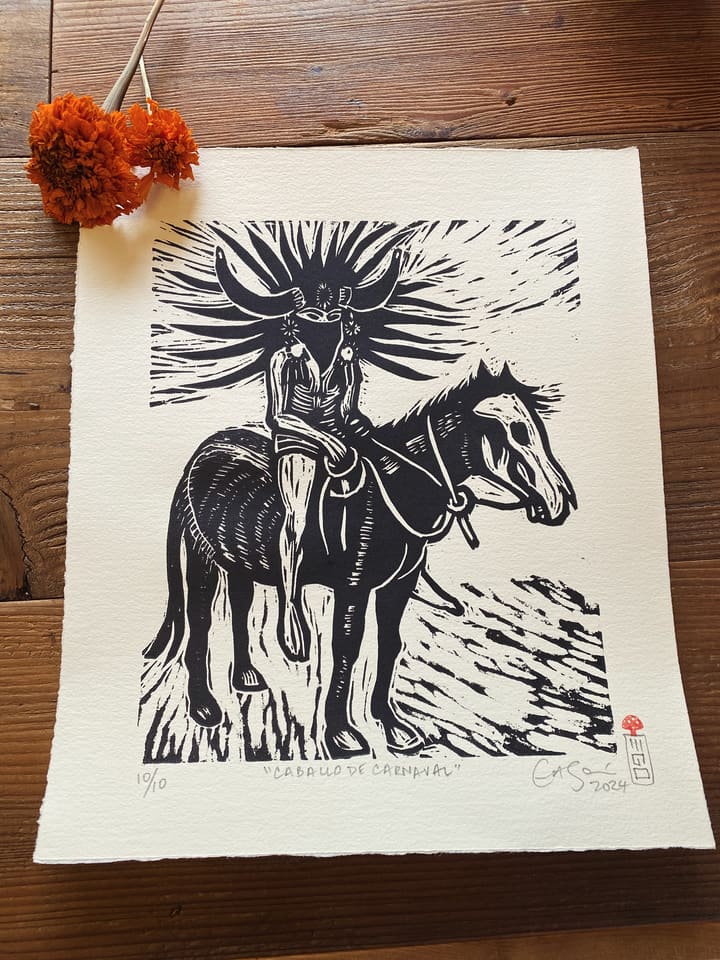 Original prints and etchings, including a linocut of a carnival horse, on rustic wood with marigolds.