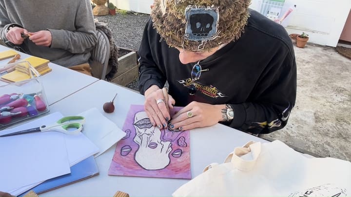 A workshop participant carving a linoleum block at a shared table in the courtyard.