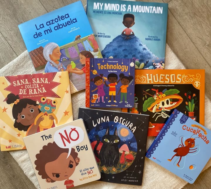 A spread of bilingual children’s books on a cream textile and sheepskin.