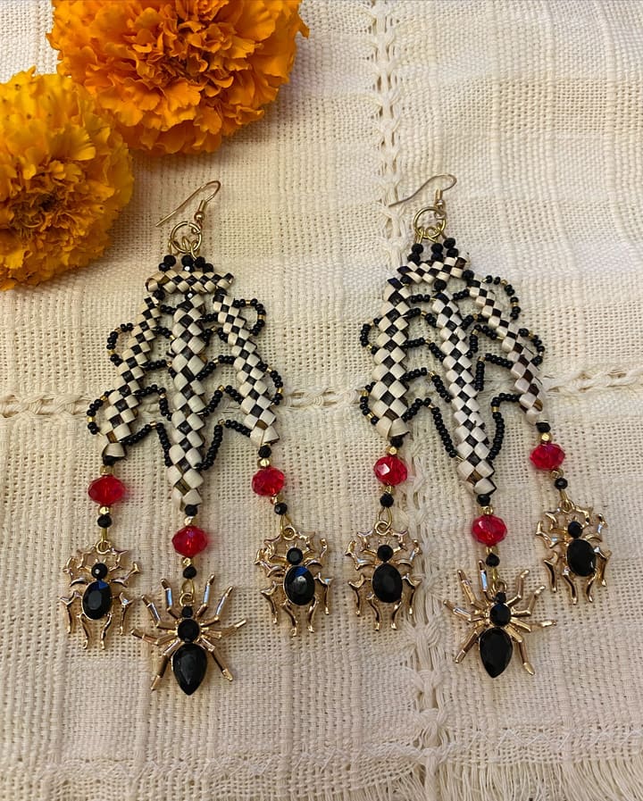 Round woven earrings of beargrass and maidenhair fern in a spider web pattern, set among marigolds.