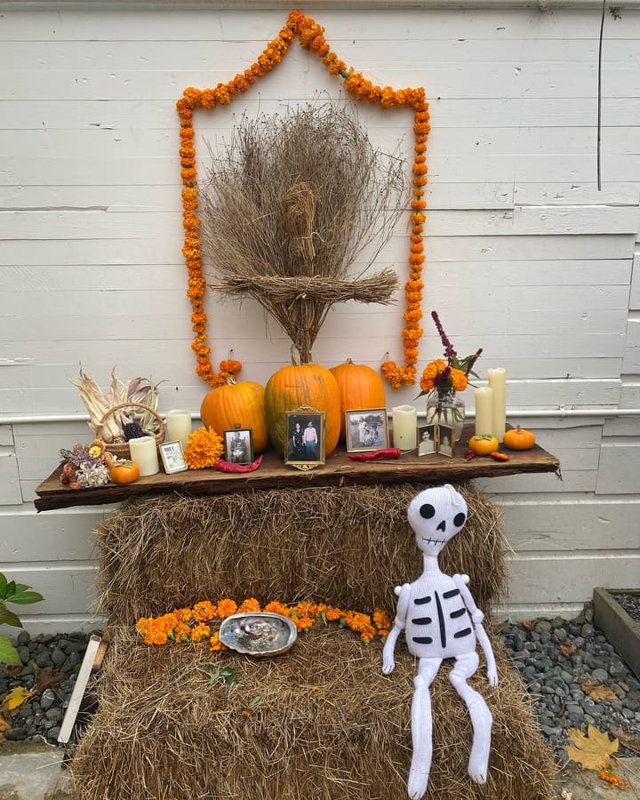 An ofrenda against the white clapboard wall: an arch of marigolds, family photos and candles.