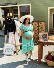 The founder beside her clothing rack and a framed painting at the Blue Lake summer market.
