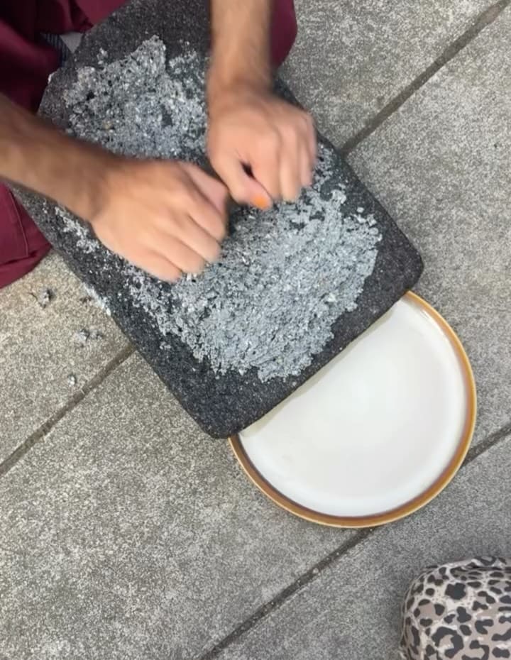 Hands grinding on a volcanic stone metate at a community dinner.