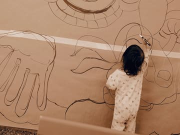 A toddler draws on the traced mural paper spread on the ground.