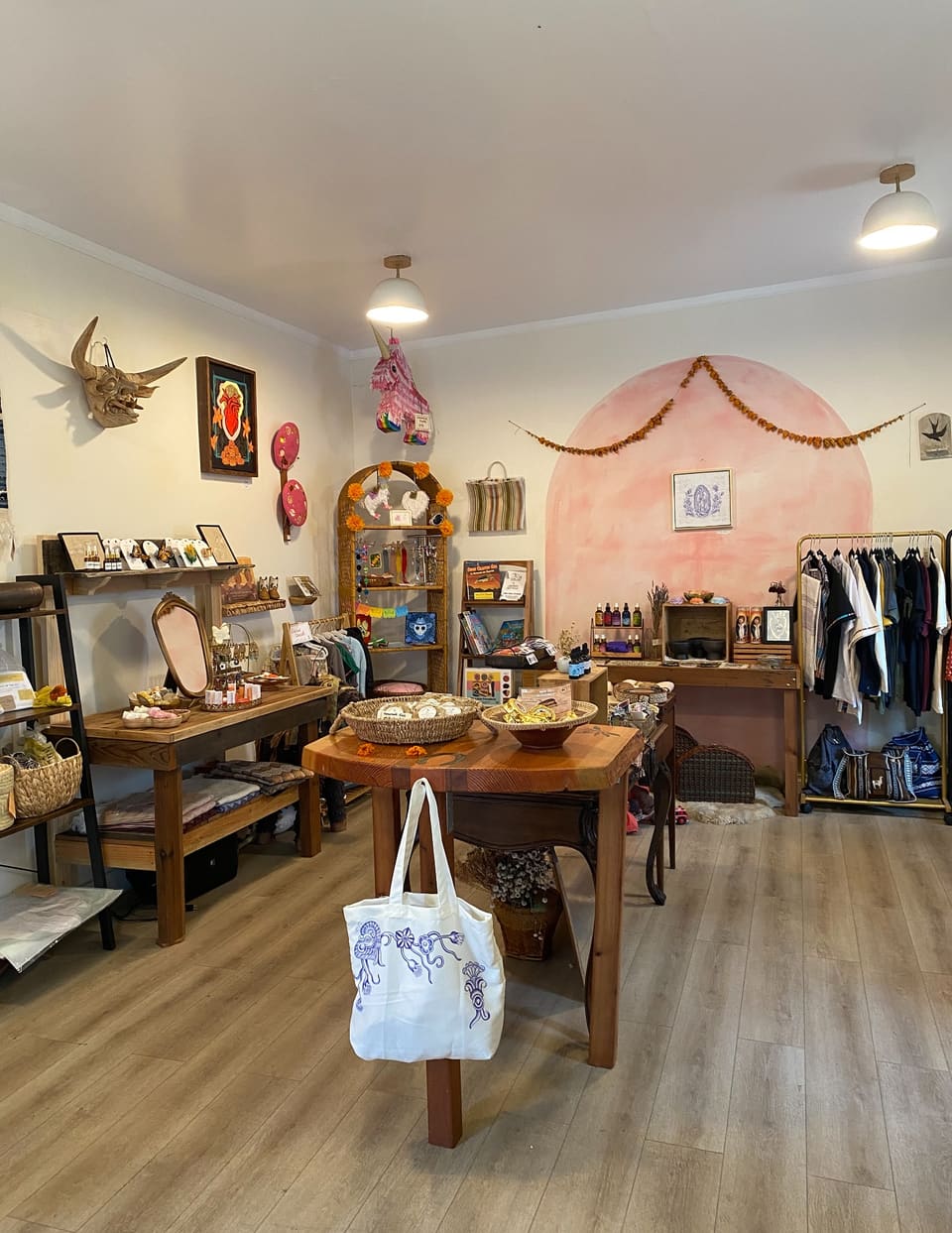 Inside La Ciendita: a pink painted arch hung with a marigold garland, wood tables of handmade soaps and jewelry, a shelf of books and a rack of clothes.