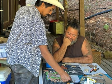 Two men planning the Nemiliztli installation over sketches at a work table.