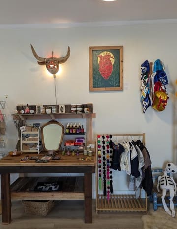 A corner of the shop wall: a steer skull, a heart painting, luchador masks and a skeleton.